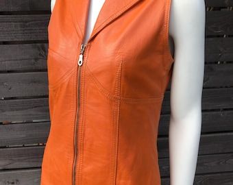 May include: Orange leather vest with a notched collar and a full-length zipper. The sleeveless vest has a tailored fit and visible stitching details. The vest is displayed on a white mannequin against a dark wooden background.