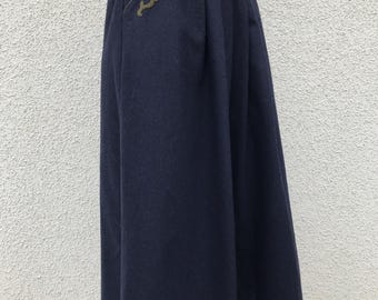 May include: Navy blue skirt with a flared silhouette. The skirt features a decorative olive green embroidered design near the pocket. The skirt is made of a thick, possibly wool, fabric.