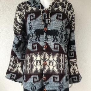 Può includere: Un cardigan con cappuccio con un motivo geometrico nei toni del grigio, marrone e bianco. Il maglione con bottoni presenta un motivo ripetuto di animali e forme stilizzate. L'indumento a maniche lunghe è esposto su un manichino.