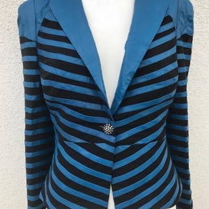 Op de afbeelding: Een blauw en zwart gestreepte blazer met een enkele knoopsluiting. De blazer heeft een V-hals en opgevulde schouders. De knoop is zilverkleurig met een decoratief ontwerp. De jas wordt getoond op een witte mannequin.
