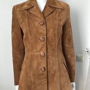 Peut inclure: Veste en daim marron clair avec un design classique. La veste présente un col cranté, quatre boutons marron et une coupe ajustée. Elle a des manches longues et une poche discrète sur le côté droit.