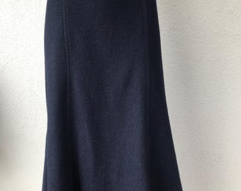 May include: A navy blue skirt with a flared hem. The skirt has a fitted waist with a decorative band and vertical seams. The fabric appears to be a soft wool or wool blend. The skirt is knee-length.