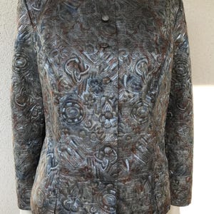 以下が含まれることがあります： グレーとブラウンの抽象的なパターンが施されたシルバーメタリックのブレザー。ブレザーはボタン留めと長袖です。