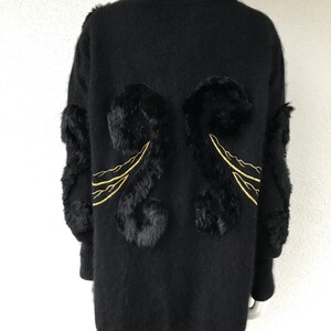 Peut inclure: Un cardigan noir en tricot à manches longues et col montant. Le cardigan est orné de broderies dorées et d'accents en fourrure noire au dos.