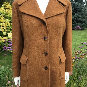 May include: A brown wool coat with a classic design. The coat features a notched collar, three buttons, and two front pockets. The coat is displayed on a mannequin. The coat's length is approximately 76 cm.