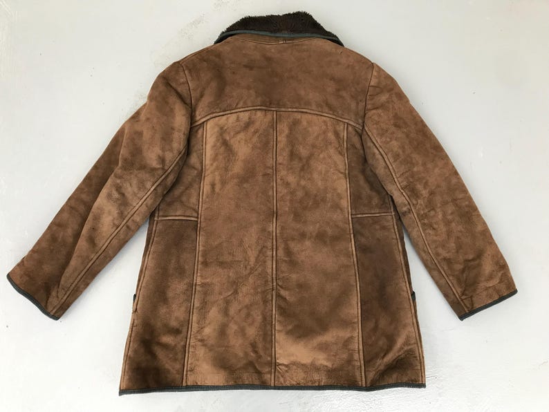 K&ouml;nnte beinhalten: Eine braune Wildlederjacke mit einem Lammfellkragen. Die Jacke hat einen Knopfverschluss und zwei Taschen.