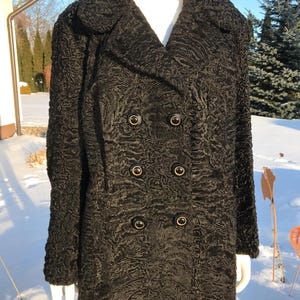 Könnte beinhalten: Ein schwarzer, doppelreihiger Mantel mit strukturierter Oberfläche und großen, runden Knöpfen. Der Mantel hat einen klassischen Kragen und scheint aus einem weichen Material zu sein. Der Mantel wird auf einer Schaufensterpuppe im Freien präsentiert.