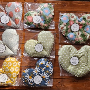 Può includere: Otto cuscinetti termici a forma di cuore in vari motivi di tessuto, tra cui stampe floreali, a pois e a fragola. Ogni cuscinetto ha un'etichetta circolare che recita "Warmth Huts".