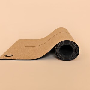 May include: A rolled up cork yoga mat with a black border. The mat has a light brown color and is rolled up tightly.