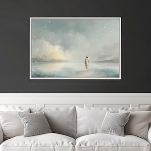 May include: A framed art print depicts a figure in a flowing robe walking on water towards the horizon. The artwork features a soft color palette of blues, whites, and beige, with a cloudy sky and subtle star details. The print is displayed above a white sofa with gray pillows.