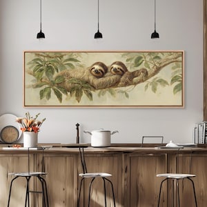 May include: A framed rectangular artwork featuring two sloths resting on a tree branch. The sloths have brown fur and are surrounded by green leaves. The artwork has a light brown wooden frame.