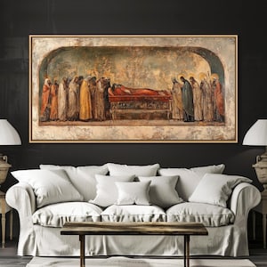 May include: A framed Renaissance-style painting depicts a religious scene with figures in robes surrounding a figure on a bed. The artwork features a gold frame and is displayed above a white sofa with pillows.
