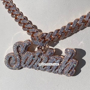 May include: A gold chain necklace with a large, custom-made pendant that says "Sasha" in sparkling diamonds. The chain is a Cuban link style and is also covered in diamonds.