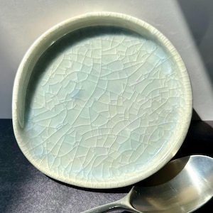 May include: A light green ceramic plate with a crackle glaze finish. The plate has a slightly rounded edge and a smooth, white interior.