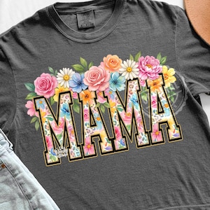 Pode incluir: Camiseta cinza escuro com a palavra "MAMA" em um design floral. As letras são preenchidas com flores coloridas e estampa de leopardo, contornadas em preto. Um arranjo floral de flores rosa, laranja e azul fica acima da palavra.