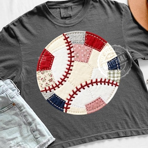 Puede incluir: Una camiseta gris oscuro con un diseño de béisbol. El béisbol está hecho de parches de tela en rojo, blanco, rosa y azul, con detalles de costura roja. La camiseta es para uso casual.