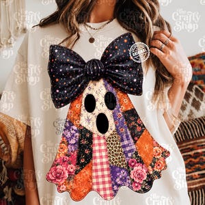 Pode incluir: Uma t-shirt de cor creme com um grande gráfico de um fantasma usando um laço preto com estrelas cor de laranja. O corpo do fantasma é composto por vários padrões de patchwork, incluindo estampados florais, manchas de leopardo e xadrez.