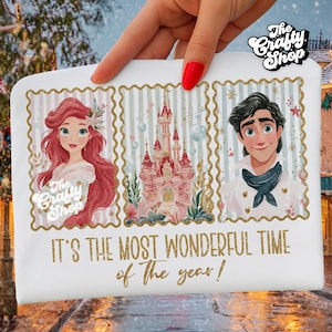 Pode incluir: Bolsa retangular branca com ilustrações de Ariel, Príncipe Eric e um castelo rosa. O texto "IT'S THE MOST WONDERFUL TIME of the year!" é impresso em dourado. O logotipo The Crafty Shop também é visível.