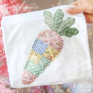 Pode incluir: Camiseta branca com uma aplicação de cenoura em patchwork. O design da cenoura incorpora padrões florais, xadrez e bolinhas em cores pastel. A parte superior da cenoura é verde. O logotipo The Crafty Shop é visível.