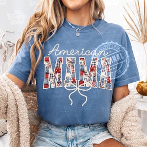 Puede incluir: Camiseta azul con las palabras "American MAMA" en blanco y letras de patchwork. Una cinta blanca est&aacute; debajo de la palabra "MAMA". La camiseta es de estilo casual.