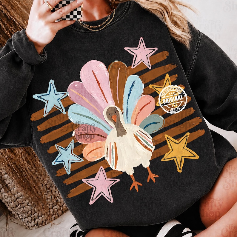 May include: A black crewneck sweatshirt featuring a central graphic of a turkey with multicoloured feathers in shades of pink, blue, and brown. The design includes brown horizontal brushstrokes, five stars in pink, blue, and yellow, and a circular logo.