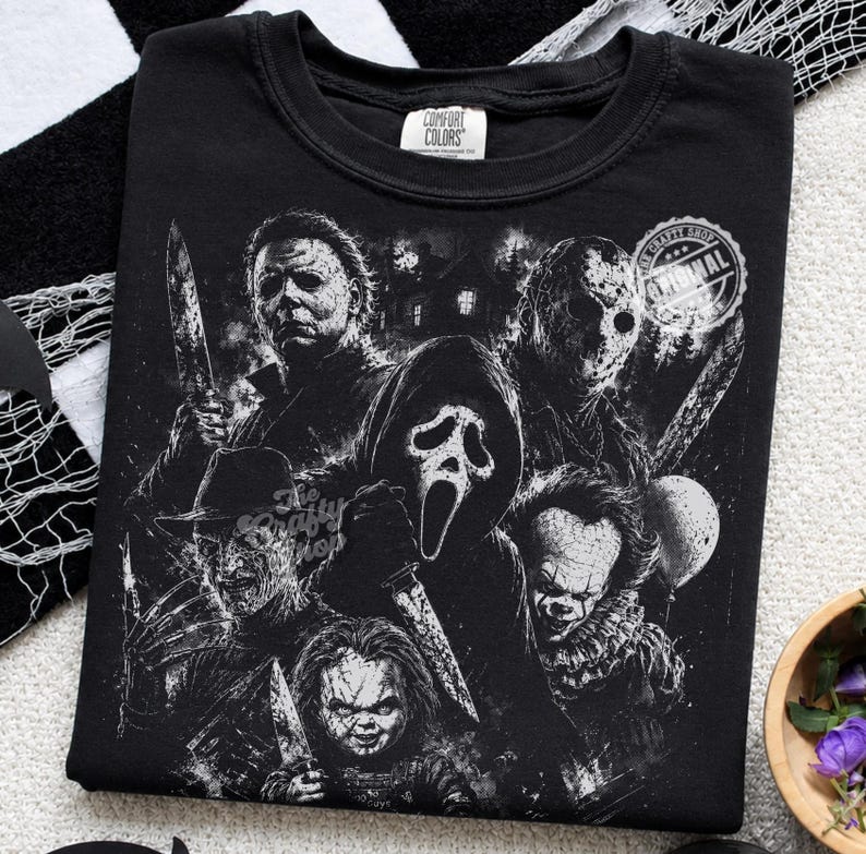 May include: A black crew neck t-shirt featuring a detailed white graphic print of various horror movie characters, including a masked figure with a knife, a hockey mask wearer, a ghost-faced figure, a clawed character, and a clown.