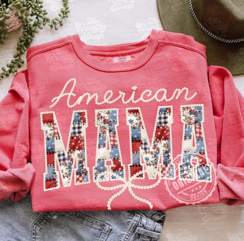Puede incluir: Una sudadera de color coral con las palabras "American MAMA" en escritura blanca y letras de patchwork. Las letras est&aacute;n decoradas con patrones de tela roja, blanca y azul. Un lazo de cuentas blanco est&aacute; debajo de la palabra "MAMA".