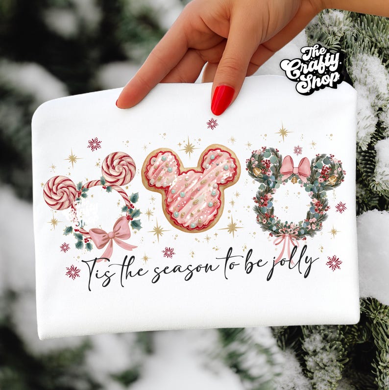 May include: White cosmetic bag with a festive design. Features three Mickey Mouse head wreaths, one with candy canes, one with a cookie design, and one with a floral wreath. The text "Tis the season to be jolly" is written across the bottom.