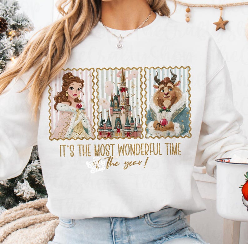Puede incluir: Sudadera blanca con un dise&ntilde;o festivo. El texto dice "IT'S THE MOST WONDERFUL TIME of the year!". El dise&ntilde;o incluye ilustraciones de Bella, la Bestia y un castillo, todo dentro de marcos decorativos. Un gran regalo navide&ntilde;o.