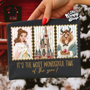 Puede incluir: Bolsa rectangular negra con un dise&ntilde;o festivo con Bella, la Bestia y un castillo. El dise&ntilde;o est&aacute; enmarcado con un fondo a rayas y el texto "IT'S THE MOST WONDERFUL TIME of The year!" est&aacute; impreso en dorado.