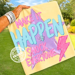 Może przedstawiać: Ż&oacute;łta koszulka z nadrukiem z napisem "MAKE IT HAPPEN SHOCK EVERYONE" w kolorze r&oacute;żowym i niebieskim. Projekt zawiera fioletową gwiazdę i r&oacute;żową błyskawicę. Koszulka ma logo "The Crafty Shop" i pieczęć "ORIGINAL DESIGN".
