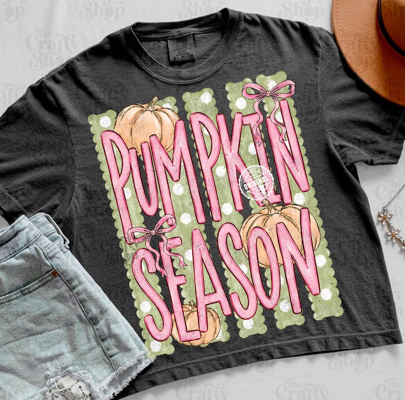 May include: A charcoal gray t-shirt featuring a graphic print with the text PUMPKIN SEASON in large pink letters. The design includes three light orange pumpkins, pink bows, and a background of vertical sage green stripes with white polka dots.