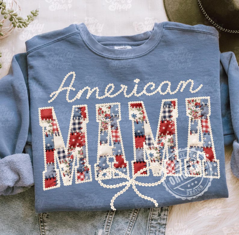 Puede incluir: Sudadera azul con la inscripci&oacute;n "American MAMA". La palabra "American" est&aacute; en escritura blanca, y "MAMA" est&aacute; en letras de patchwork con patrones rojos, blancos y azules. Una cinta blanca est&aacute; debajo de la palabra "MAMA".