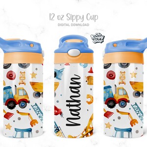 Puede incluir: Un vaso de 12 onzas de color azul y naranja con tapa de pajita. El vaso tiene un fondo blanco con un patr&oacute;n de veh&iacute;culos de construcci&oacute;n y el nombre "Nathan" impreso en &eacute;l.