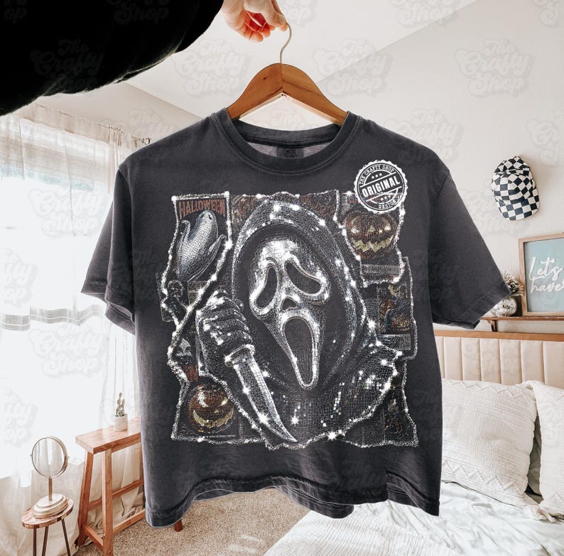 May include: A charcoal gray short-sleeve t-shirt featuring a graphic print of a hooded figure holding a knife, surrounded by Halloween-themed imagery including pumpkins and corn. A circular white label with the text Original is on the chest.