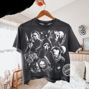 May include: A charcoal gray short-sleeve t-shirt featuring a white graphic print of various horror movie characters, including Michael Myers, Jason Voorhees, Ghostface, Pennywise, and Chucky, all holding knives or weapons.