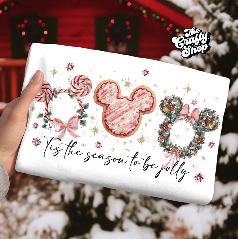 May include: White holiday-themed towel featuring three Mickey Mouse-shaped designs: a candy cane wreath, a pink frosted cookie, and a floral wreath. The text "'Tis the season to be jolly" is written in cursive. The Crafty Shop logo is in the upper right corner.