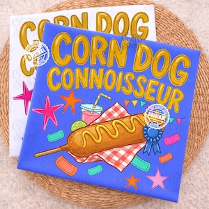 Op de afbeelding: Een blauw stoffen vierkant met de gele tekst CORN DOG CONNOISSEUR boven een afbeelding van een corn dog met mosterd, een drankje, een rood-wit geblokt servet, een blauw lint, kleurrijke sterren en kleine rechthoekige kaartjes eromheen.