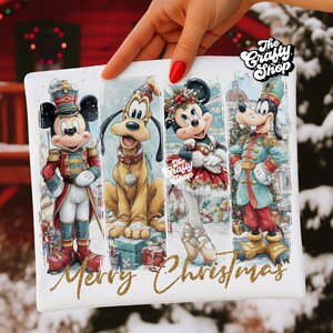May include: A white rectangular Christmas-themed print featuring Mickey Mouse, Pluto, Minnie Mouse, and Goofy in festive attire. The words "Merry Christmas" are written in gold glitter. The Crafty Shop logo is visible.
