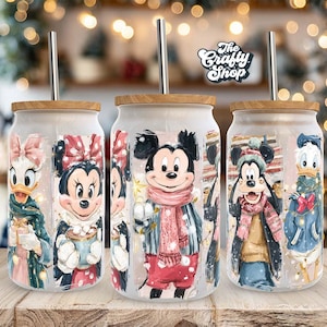 May include: Three glass tumblers with wooden lids and stainless steel straws. Each tumbler features a different Disney character in winter attire: Daisy Duck, Minnie Mouse, Mickey Mouse, Goofy, and Donald Duck. The Crafty Shop logo is visible.