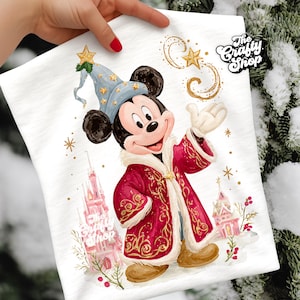 May include: White t-shirt featuring a colorful illustration of Mickey Mouse dressed as a wizard, wearing a blue hat and red robe. The design includes gold stars and the text "The Crafty Shop".