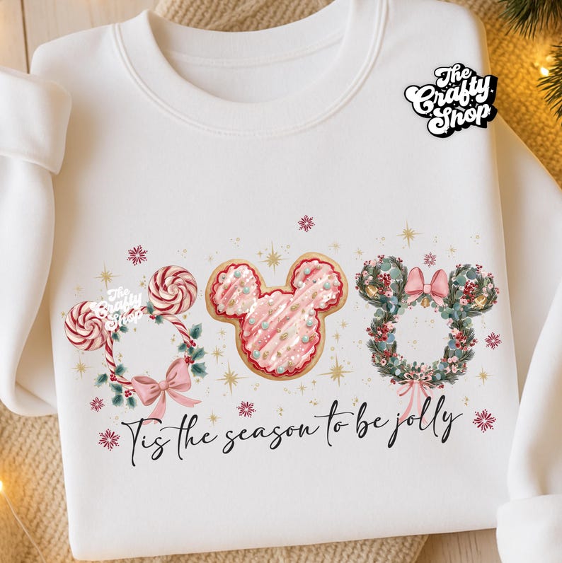 May include: White sweatshirt with a festive design featuring three Mickey Mouse head shapes. One is a candy cane wreath, one a pink cookie, and the last a floral wreath. The text "Tis the season to be jolly" is below the designs.