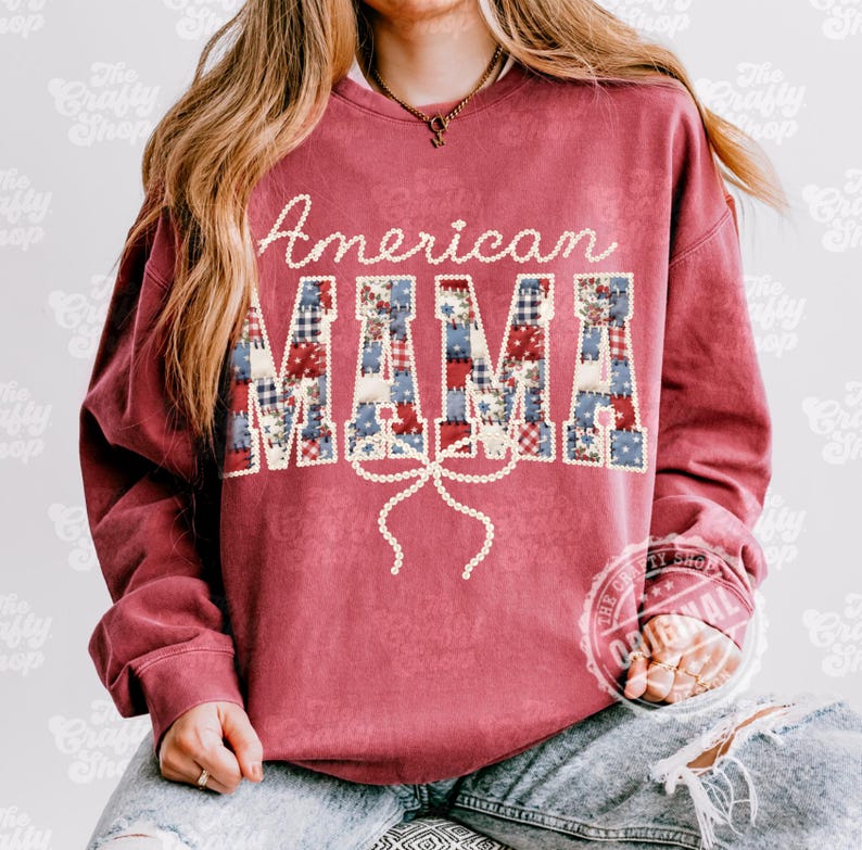 Puede incluir: Una sudadera granate con las palabras "American MAMA". La palabra "American" est&aacute; escrita en blanco, y "MAMA" est&aacute; en letras de patchwork con patrones rojos, blancos y azules. Un lazo blanco est&aacute; debajo.