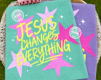 Peut inclure: Un t-shirt sarcelle avec le texte jaune JESUS CHANGES EVERYTHING et des étoiles roses, superposé sur un t-shirt violet avec des graphismes similaires. Une pince à cheveux rose clair est posée au-dessus. Chaque t-shirt porte un logo circulaire.