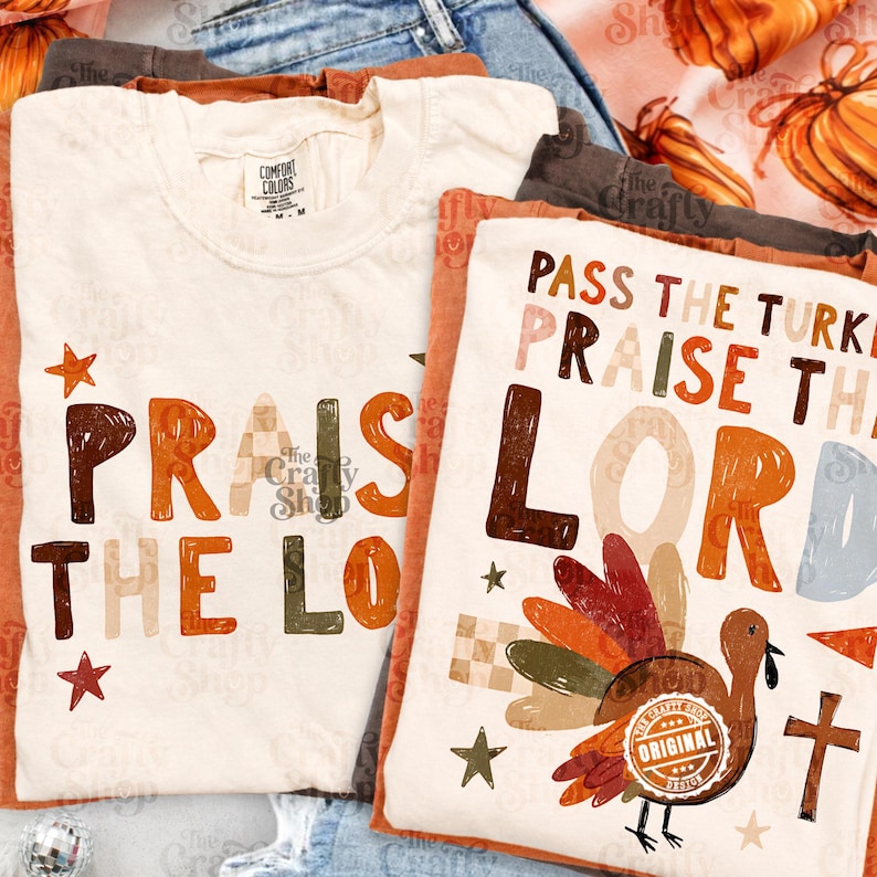Peut inclure: Deux t-shirts blanc cass&eacute; avec des graphismes sur le th&egrave;me de l'automne. L'un affiche le texte "PRAISE THE LORD" en lettres marron, orange et &agrave; carreaux avec des &eacute;toiles. L'autre pr&eacute;sente "PASS THE TURKEY PRAISE THE LORD" avec une dinde et une croix.