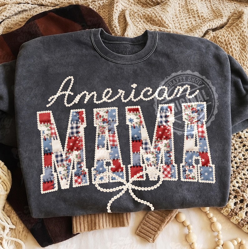 Puede incluir: Sudadera gris oscuro con las palabras "American MAMA" en letras blancas y patchwork. Las letras est&aacute;n decoradas con tela roja, blanca y azul. Un lazo de cuentas blanco est&aacute; debajo de la palabra "MAMA".