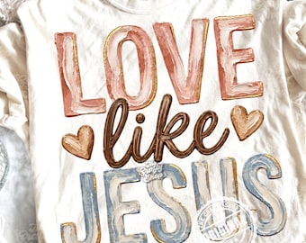 Peut inclure: T-shirt Comfort Colors crème avec l'inscription "LOVE like JESUS" dans un style aquarelle. Le mot "LOVE" est rose avec des bordures dorées, "like" est marron et "JESUS" est bleu avec des bordures dorées. Deux graphiques de cœur sont également inclus.