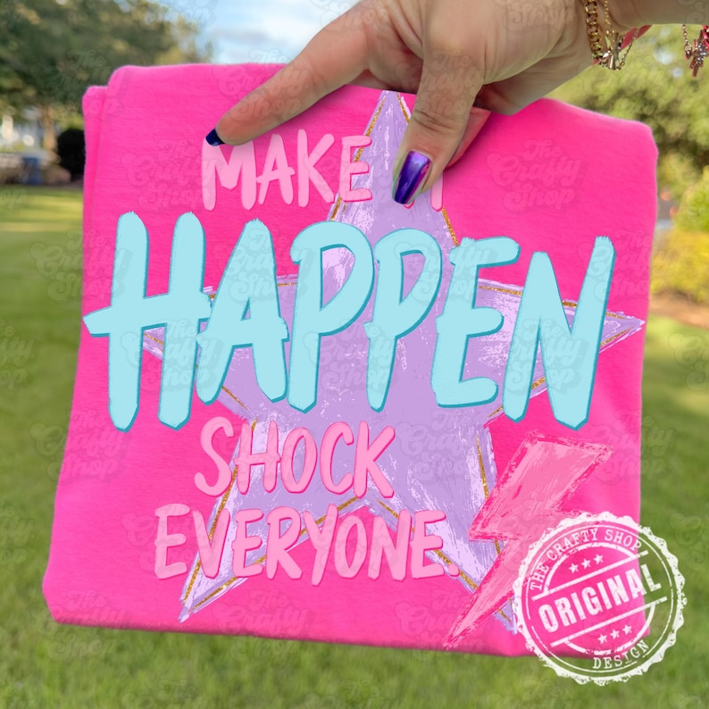 Może przedstawiać: Jasnor&oacute;żowa koszulka z napisem "MAKE IT HAPPEN SHOCK EVERYONE" w jasnoniebieskiej i r&oacute;żowej czcionce. Na koszulce znajduje się r&oacute;wnież grafika gwiazdy i błyskawicy. Koszulka jest trzymana przez dłoń.