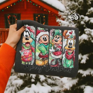 Puede incluir: Sudadera gris oscuro con un dise&ntilde;o navide&ntilde;o colorido con personajes de dibujos animados. El dise&ntilde;o incluye a Goofy, Mickey Mouse, Minnie Mouse y Pluto, todos vestidos con atuendos festivos. Las palabras "Merry Christmas" est&aacute;n escritas en la parte inferior.