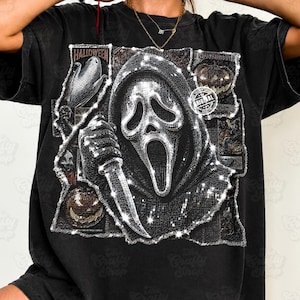 May include: A black t-shirt featuring a large, central graphic of a hooded figure with a mask holding a knife. The design includes smaller rectangular panels with Halloween-themed imagery, including pumpkins and corn, and a circular stamp reading ORIGINAL.